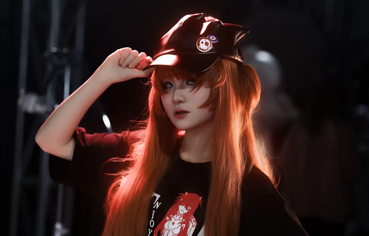 A young adult posing in cosplay attire with a cap and vibrant red hair under studio lights.