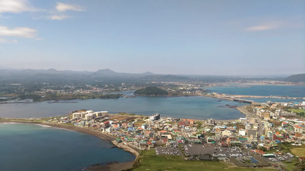 Aerial view of Seogwipo, Jeju-do, showcasing coastal cityscape and serene sea.