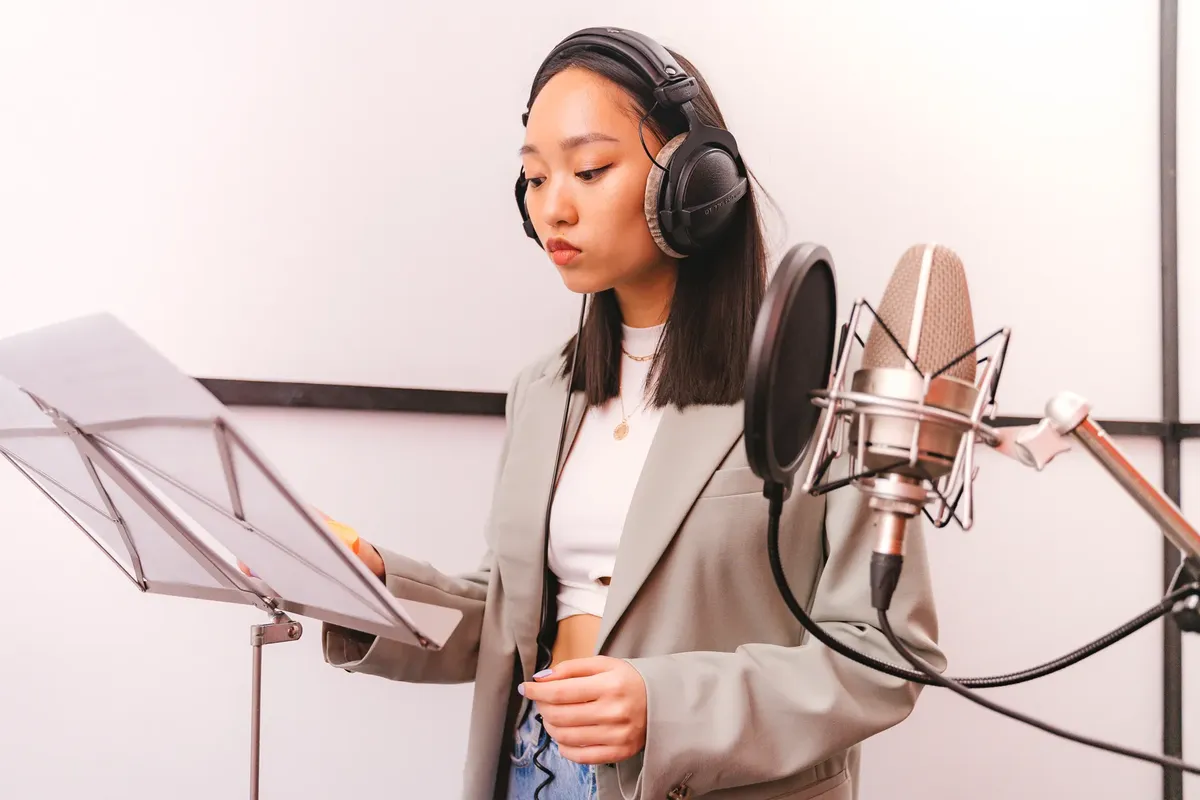 Asian woman wearing headphones recording in music studio with microphone.
